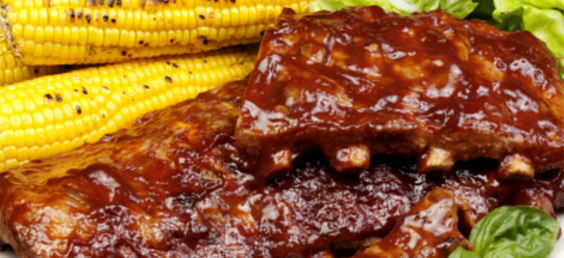 A close up of some ribs and corn on the cob