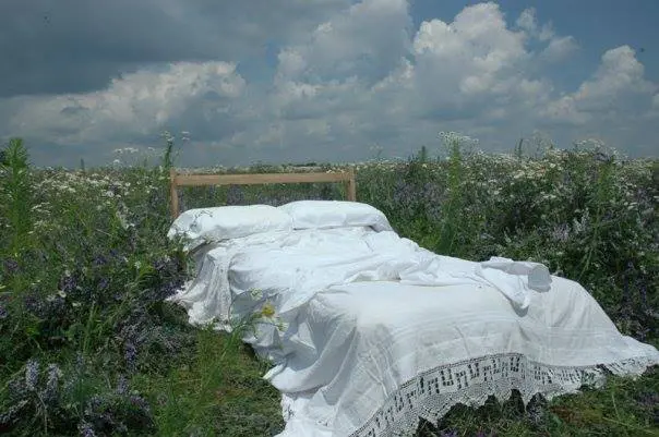 A bed in the middle of a field covered with white sheets.