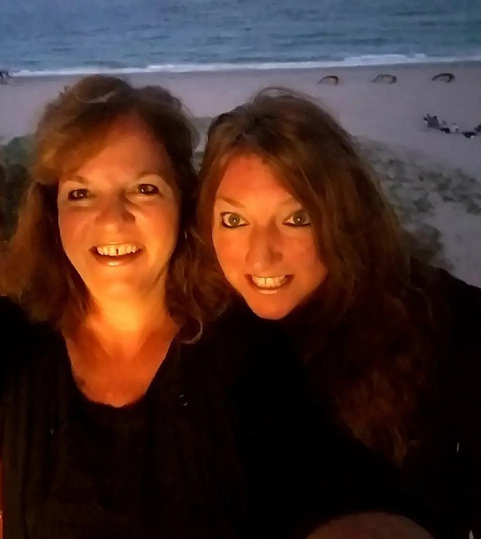Two women standing next to each other on a beach.